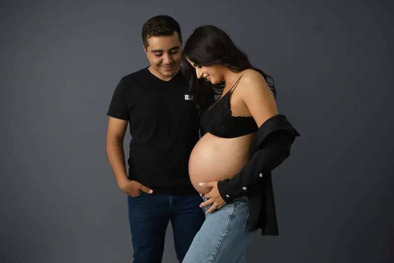 Casal vestindo roupas pretas e jeans sob fundo cinza em ensaio gestante atemporal
