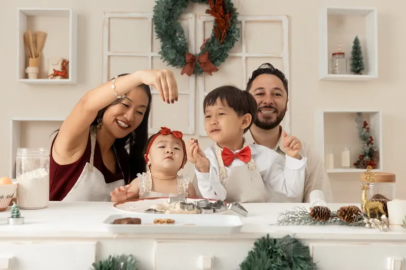 Família junta na cozinha temática preparando biscoitos em momento divertido do ensaio de Natal